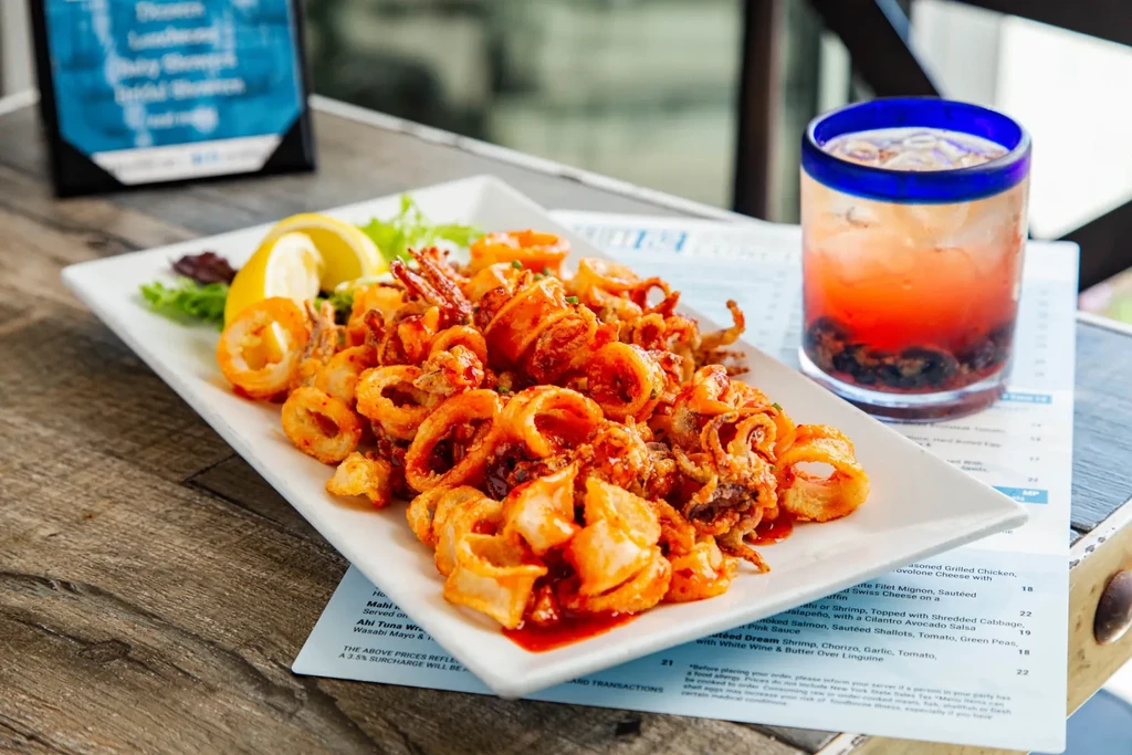 A plate of fried calamari with lemon and a layered drink on a table.