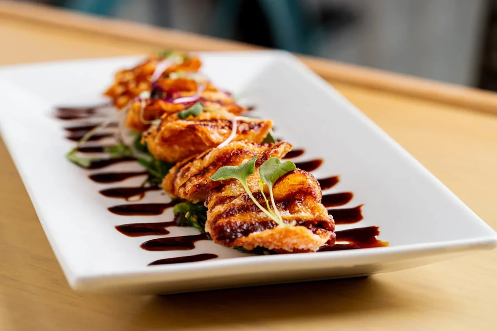 Five fried dumplings on a white plate with sauce and garnish.