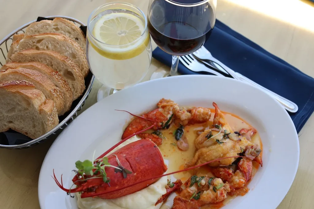 A plate of lobster with mashed potatoes, bread, and drinks.