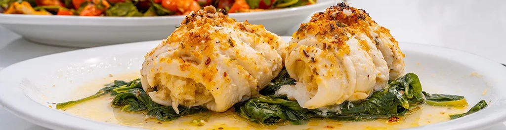 Two baked stuffed fish fillets with spinach and sauce on a white plate.