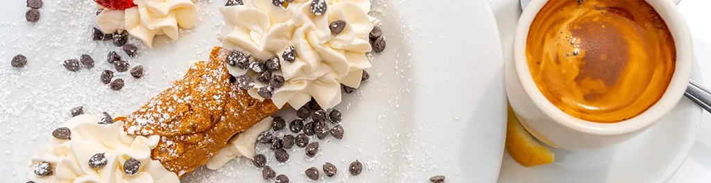 Cannoli, whipped cream, chocolate chips, and espresso on a white plate.