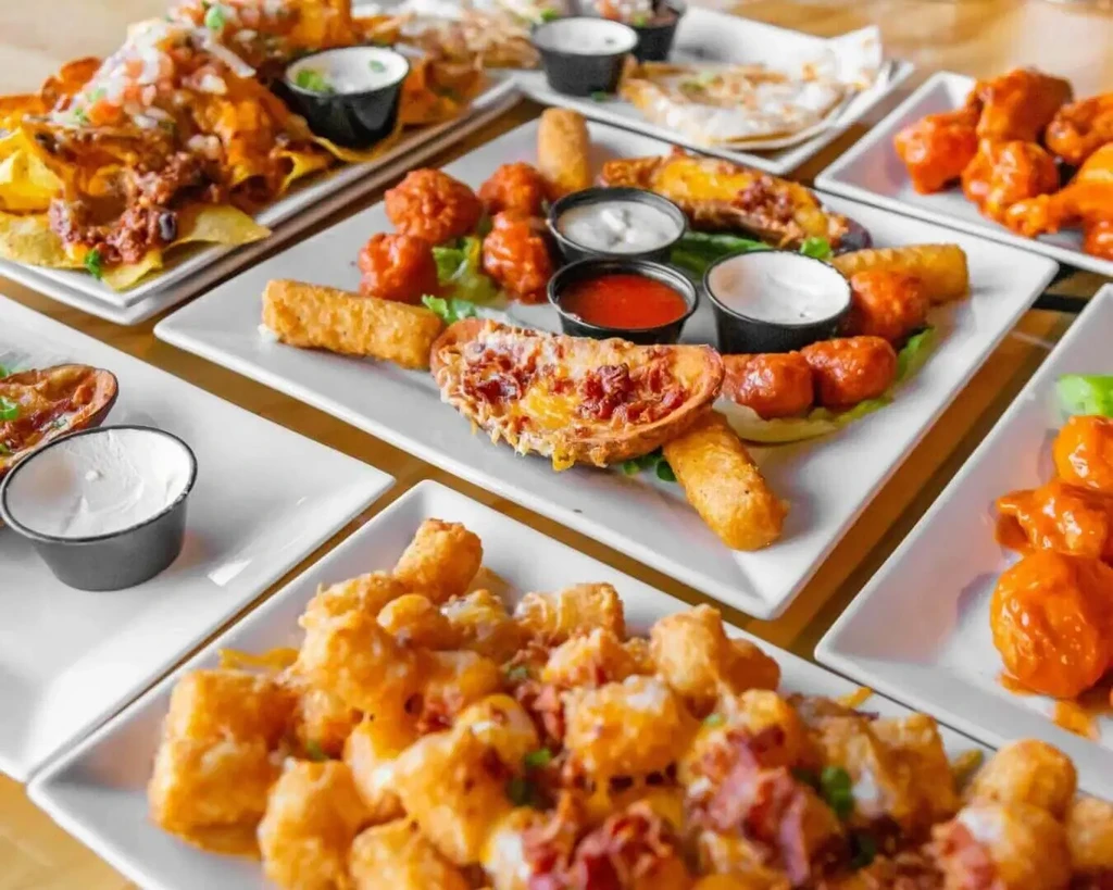A table filled with plates of various appetizers like nachos, wings, and tots.