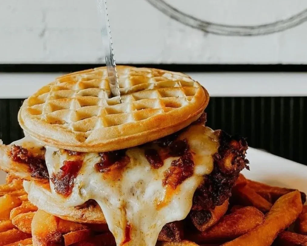 Close-up of a waffle sandwich with melted cheese and fries on a plate.
