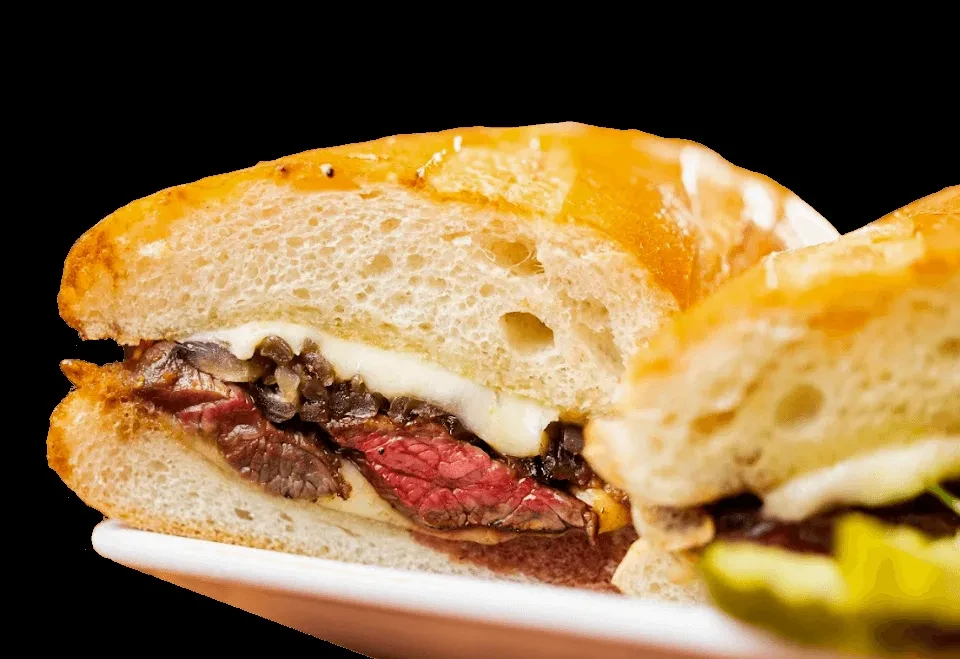 Close-up of a cut steak sandwich with caramelized onions and melted cheese.