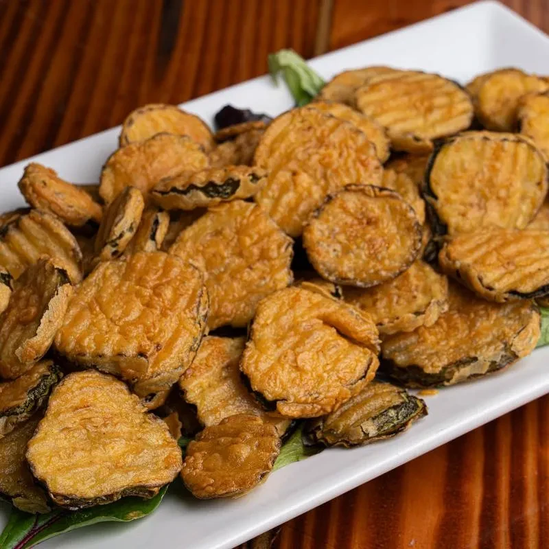 A white plate filled with golden-brown fried pickles and a few lettuce leaves.
