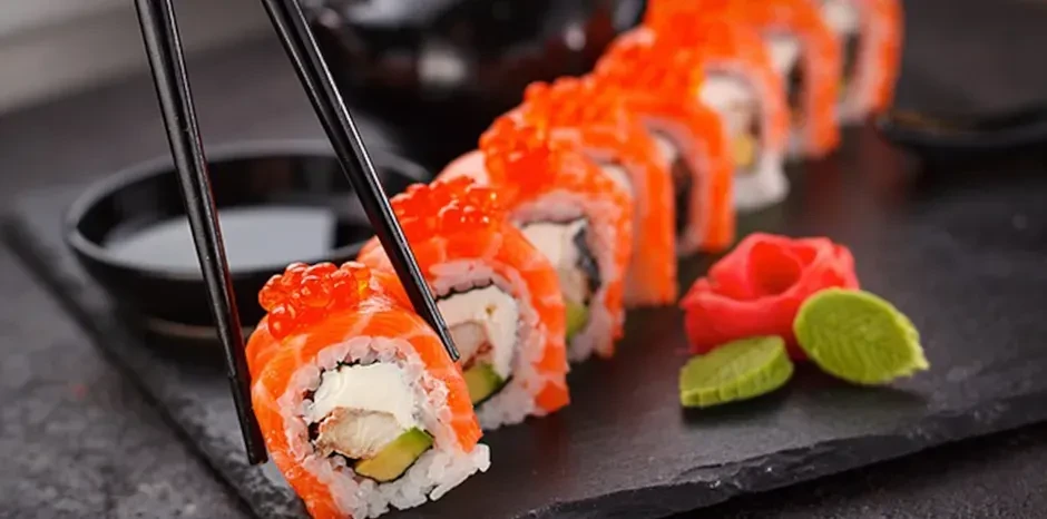 Chopsticks pick up salmon sushi with fish roe, wasabi, and ginger.