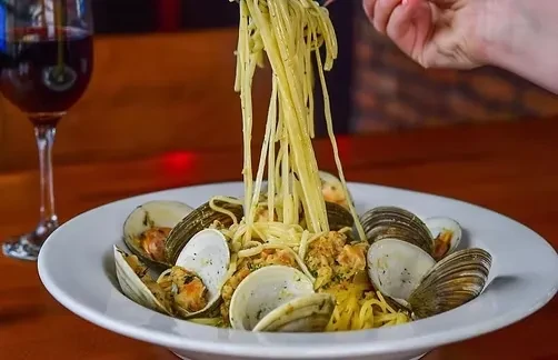Hand lifting spaghetti with clams and red wine.