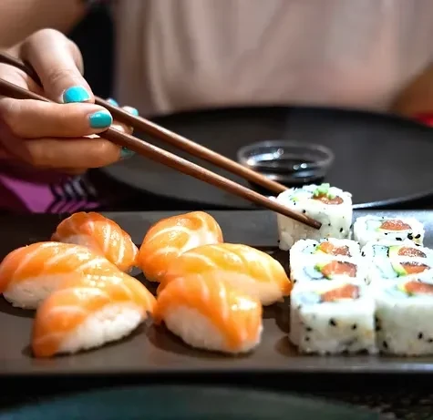Chopsticks hold a sushi roll over a plate of sushi and sashimi.