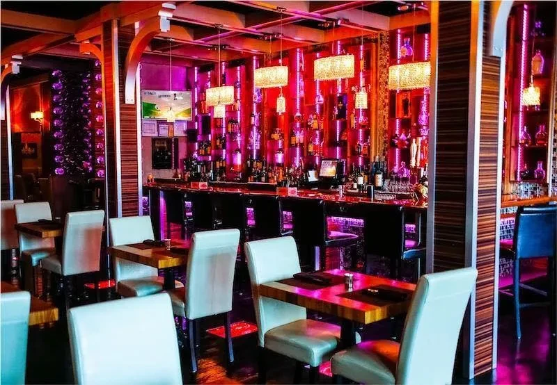 A bar and restaurant with pink lighting and bottles on shelves.