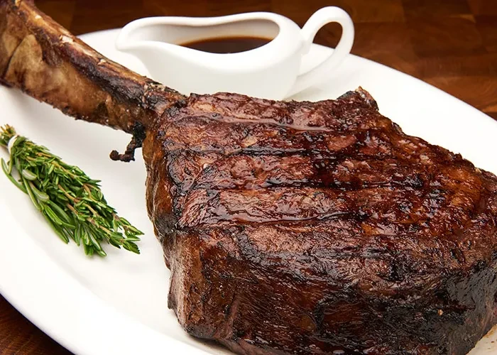 Grilled tomahawk steak, gravy, and herbs on a white plate.