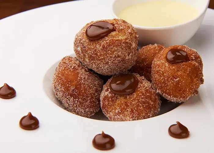 Sugar-dusted donut holes with caramel dots on a white plate.