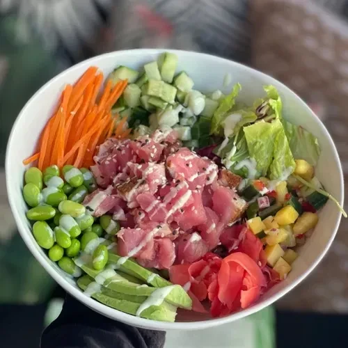 A white bowl filled with poke, tuna, avocado, vegetables, and dressing.