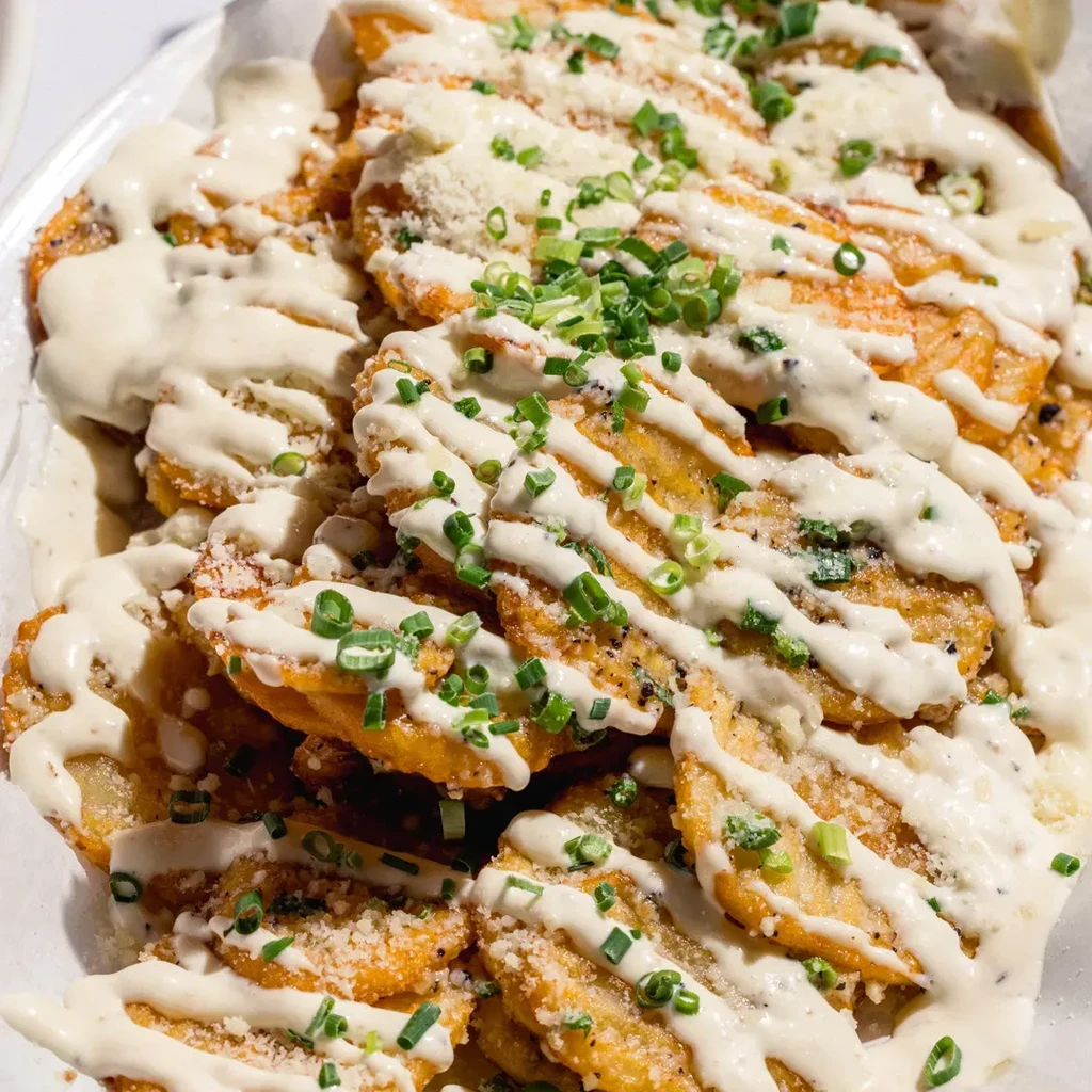 A plate of golden fried plantains drizzled with sauce and topped with chives.