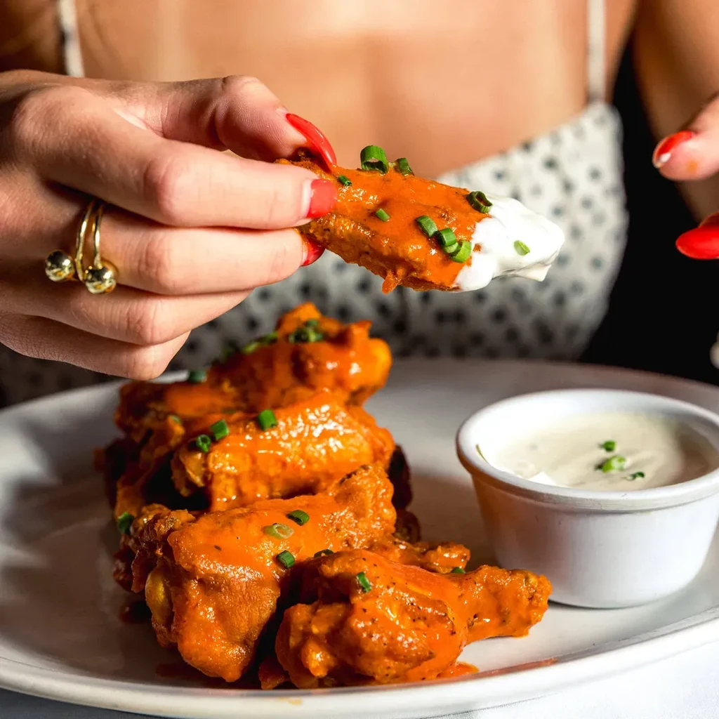 A person dips a buffalo wing into white sauce.