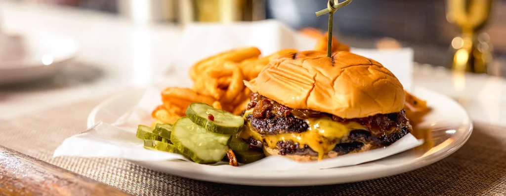 A double cheeseburger with caramelized onions, pickles, and curly fries.