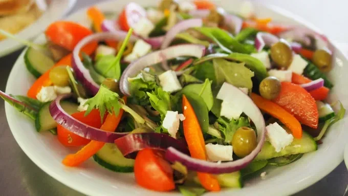 A colorful salad with lettuce, tomatoes, cucumbers, onions, olives, and feta.
