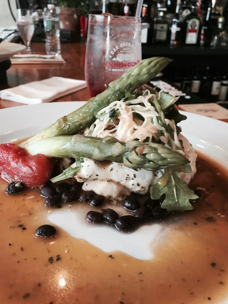 A plate of food with asparagus, fish, black beans, and red sauce.