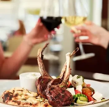 Plate of lamb chops, naan, and salad with people toasting wine.
