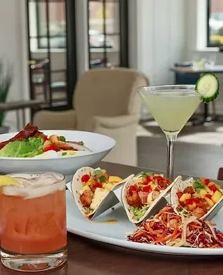 Shrimp tacos, cocktails, and another dish on a restaurant table.