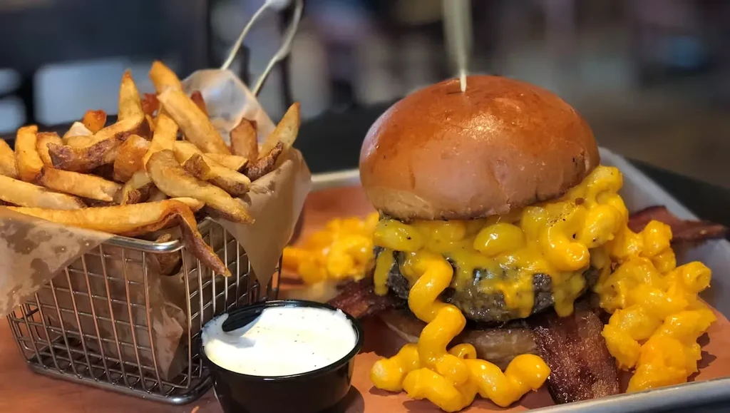 A burger with mac and cheese, bacon, and a side of fries.