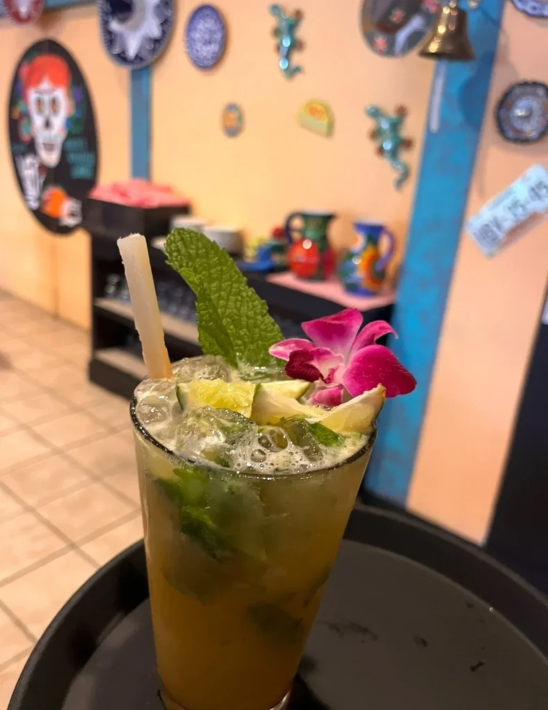 A tall glass of mojito with mint, lime, and a pink orchid.