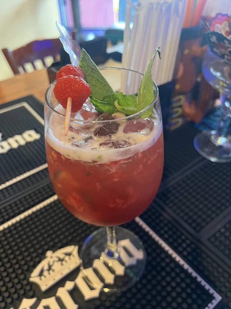Red cocktail with raspberries and mint leaves on a bar mat.
