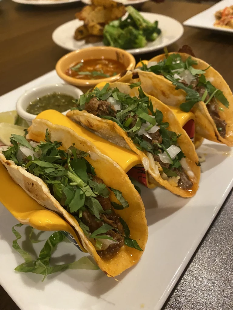 Four tacos with meat, cheese, cilantro, and onion on a white plate.