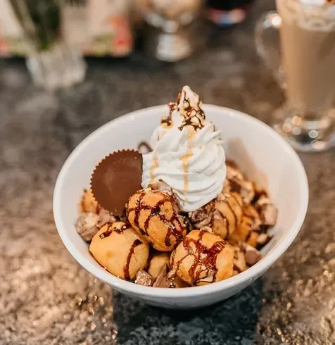 A white bowl of churro bites topped with whipped cream and chocolate sauce.