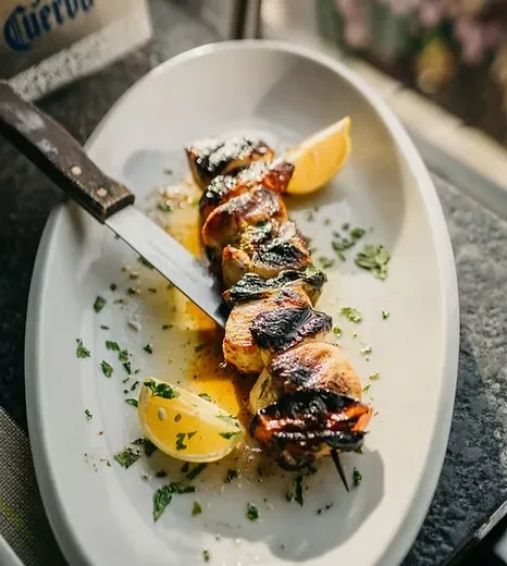 Charred chicken skewer with lemon slices and parsley on a white platter.