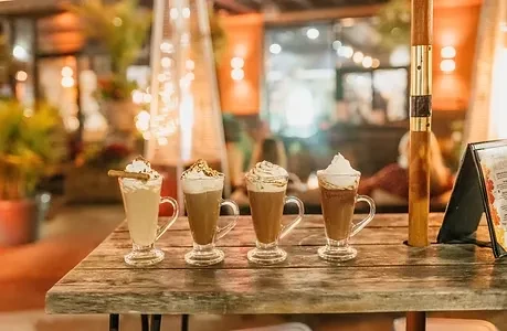 Four festive drinks with whipped cream on an outdoor wooden table.