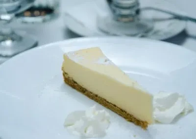A slice of plain cheesecake with whipped cream on a white plate.