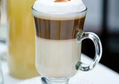 A layered coffee drink in a clear glass mug with foam and cinnamon.
