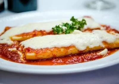 Two cannelloni covered with tomato sauce, mozzarella cheese, and parsley.