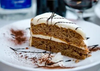 A slice of carrot cake with white frosting and chocolate drizzle.