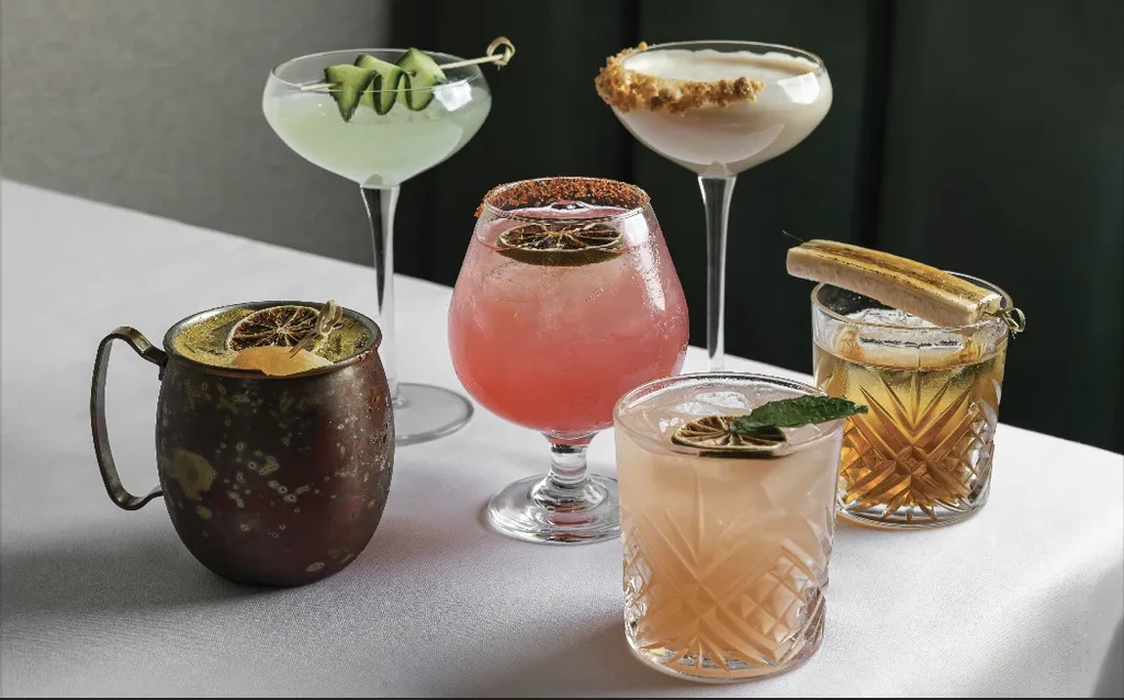 A table of six colorful, garnished cocktails in various glasses.