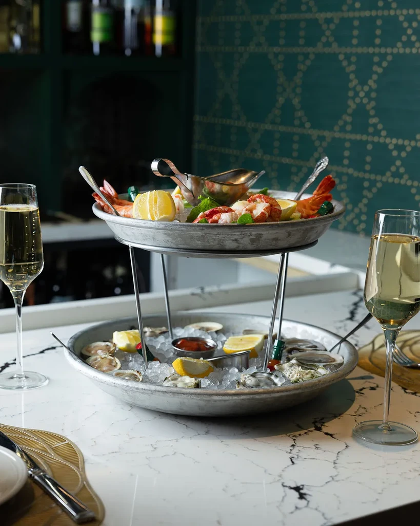 Seafood tower with shrimp and oysters, champagne flutes, at a bar.