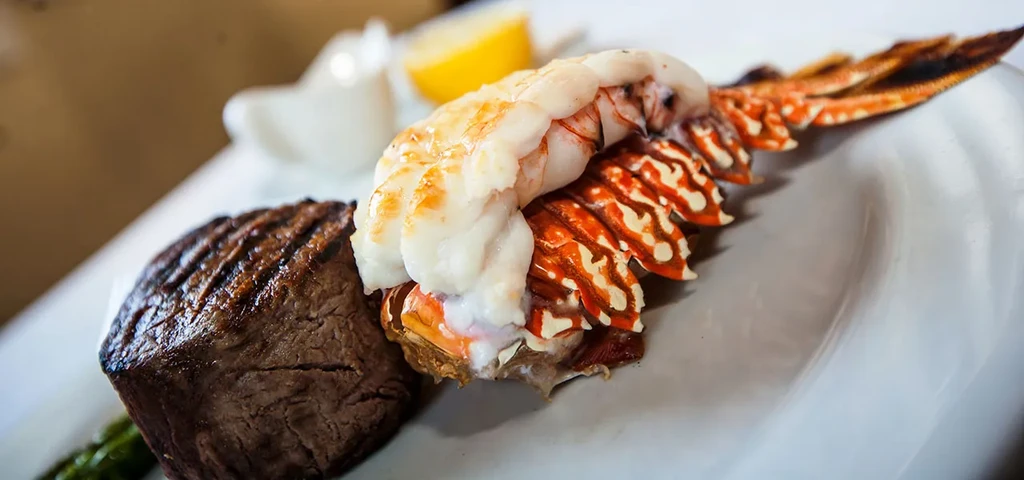 Plate with steak, asparagus, and lobster tail with a lemon wedge.