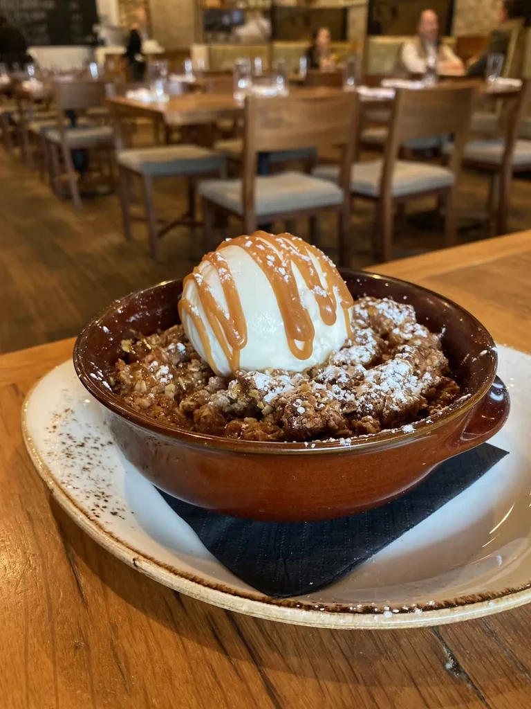Apple crumble with vanilla ice cream and caramel sauce on a table.