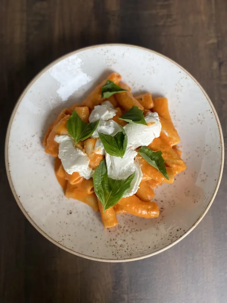 Pasta with orange sauce, burrata, and basil in a white bowl.