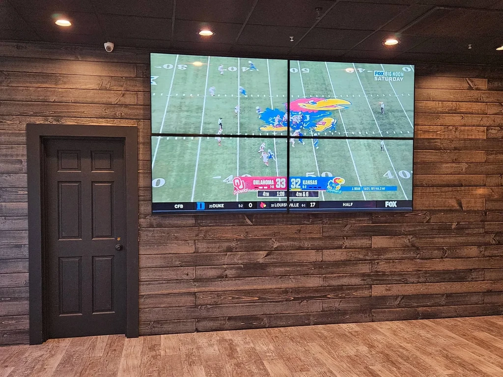 Video wall showing a football game on a wooden-paneled wall next to a door.