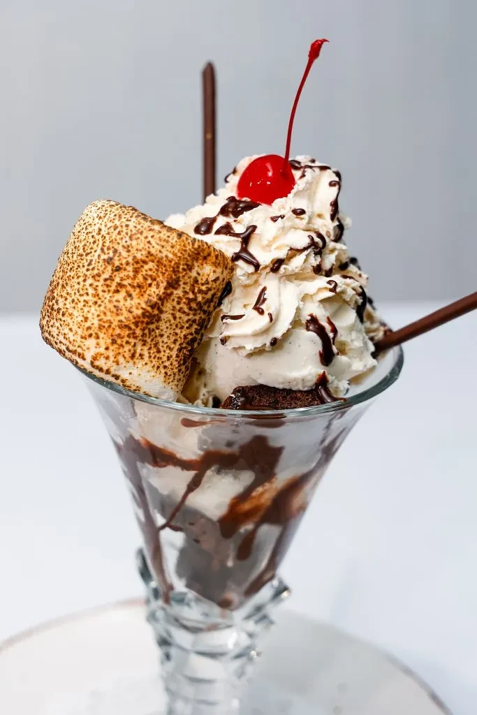 Dessert in a glass with toasted marshmallow, whipped cream, and a cherry.