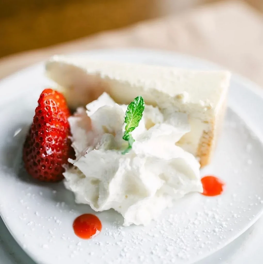 Slice of cheesecake with whipped cream, strawberry, and mint.