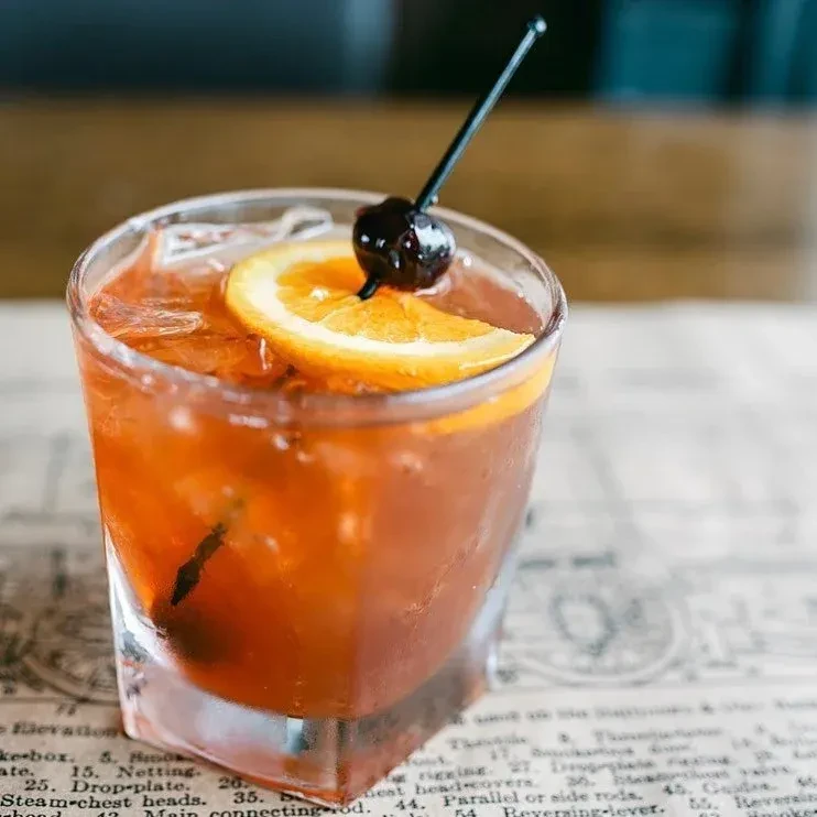 An Old Fashioned cocktail garnished with an orange slice and cherry.