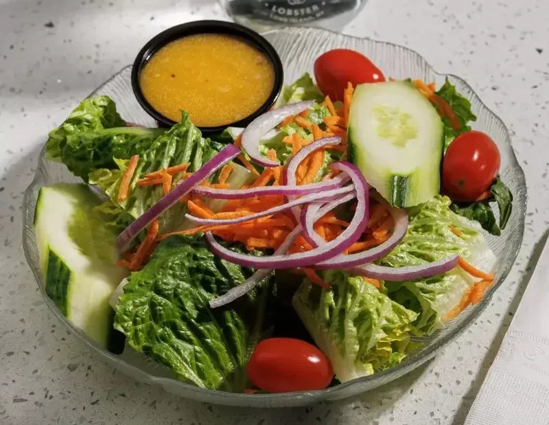 A garden salad with lettuce, tomatoes, cucumber, carrots, onions, and dressing.