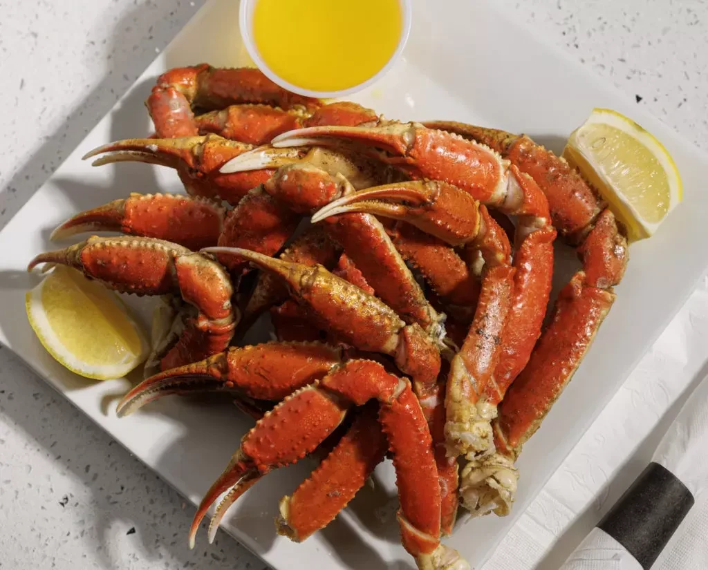 A plate of cooked crab legs, lemon wedges, and a side of butter.