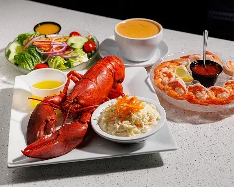 A cooked lobster, shrimp cocktail, salad, and soup on a white table.