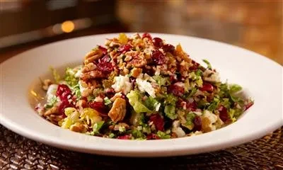 A white plate of salad with lettuce, nuts, and cranberries.