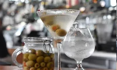 A martini with olives, a glass of water, and a jar of olives.