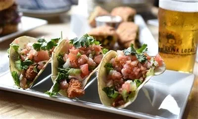 Three tacos with meat, pico de gallo, and cilantro on a white plate.