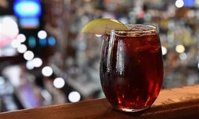 A stemmed glass of red drink with ice and a green apple slice.